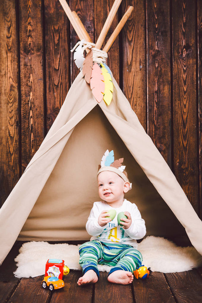 Criança, menino, brincando na tenda dentro de casa em um fundo de madeira. Vestido em indiano
 - Foto, Imagem