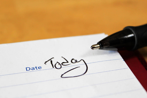 A closeup of the notepad with a pen tip and the words today written for the date - Photo, Image