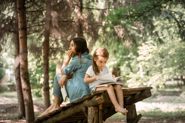 äiti ja tytär lukevat kirjaa puistossa
 - Valokuva, kuva