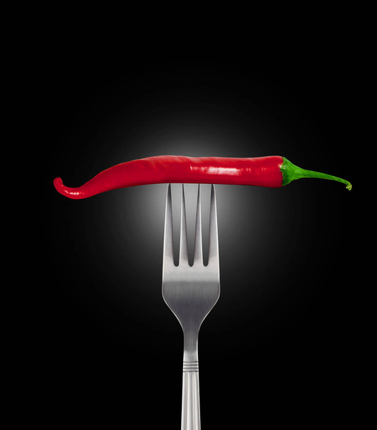 Red hot chili pepper speared onto metal fork shot on black backg - Foto, Imagen
