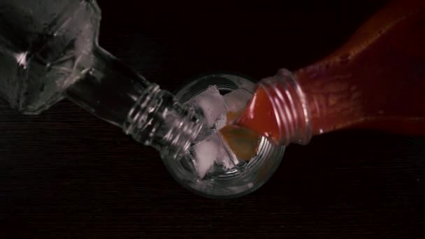 Movimento lento. Despeje simultaneamente o suco e a vodka em um copo com vista superior do gelo
 - Filmagem, Vídeo