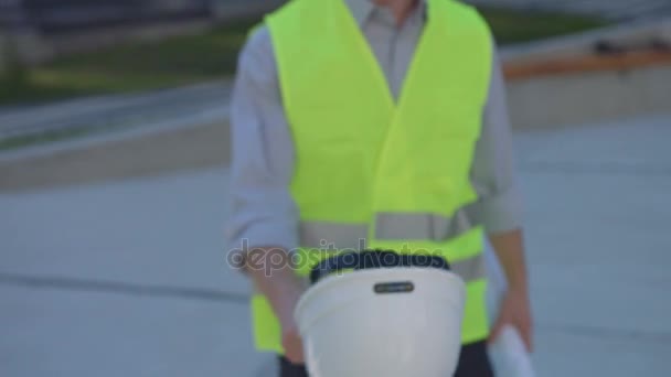 Caucasian builder with rousse hair and beard putting on head white protective helmet and looking drawing on the background built house. Close up. - Imágenes, Vídeo