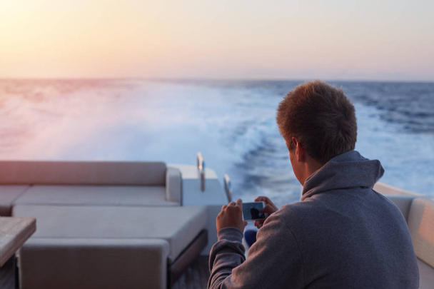 Задний план кавказского мужчины собирается сфотографировать великолепный закат на современной роскошной яхте. Человек удаляет старые фотографии со своего телефона, чтобы запечатлеть живописный вид морской жизни
. - Фото, изображение