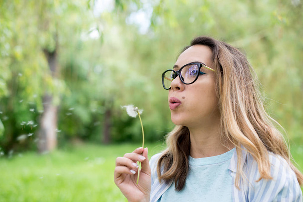 Portrait of beautiful young woman blowing dandelion flower - Foto, imagen