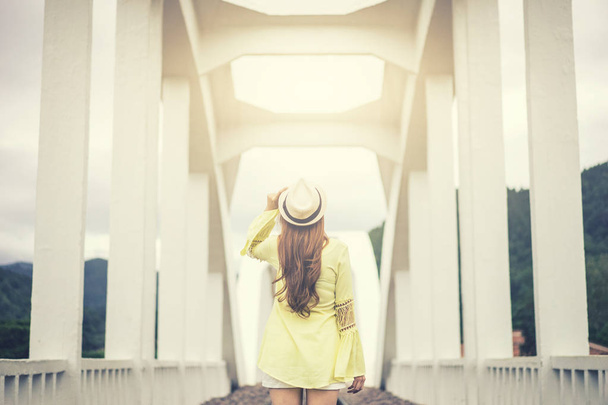 wanderlust mujer joven sosteniendo sombrero con fondo de puente blanco
, - Foto, Imagen