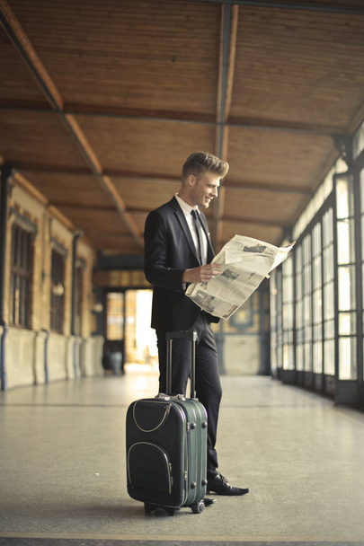 Young businessman with suitcase reading newspaper  - Φωτογραφία, εικόνα