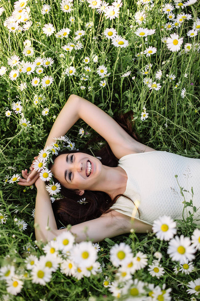 Beautiful woman enjoying daisy field, nice female lying down in meadow of flowers, pretty girl relaxing outdoor, having fun, holding plant, happy young lady and spring green nature, harmony concept - Valokuva, kuva