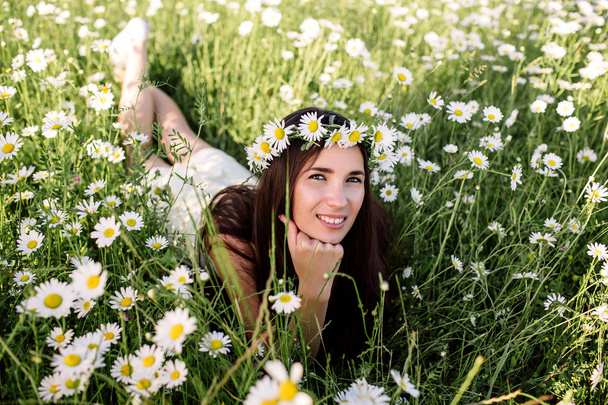 Belle femme appréciant le champ de marguerite, belle femelle couchée dans la prairie de fleurs, jolie fille se relaxant en plein air, s'amusant, tenant la plante, jeune dame heureuse et printemps nature verte, concept d'harmonie - Photo, image