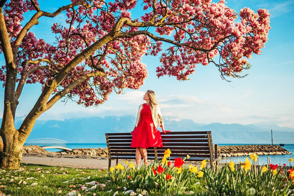 Jeune femme blonde admirant une vue imprenable sur le lac Léman, Suisse. Femme assise sur le banc sous un magnolia fleuri
 - Photo, image