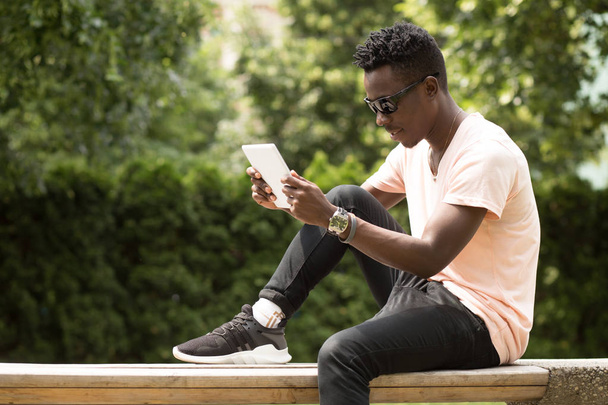 Black man using white tablet PC in park - Fotó, kép