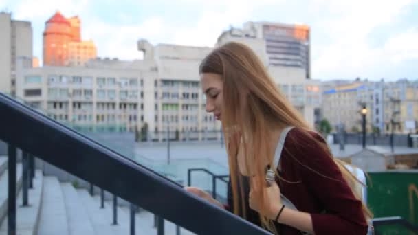 Aantrekkelijk meisje in een rode jas met rode lippen gaat door de straat van een stad dan draait camera en glimlach. - Video