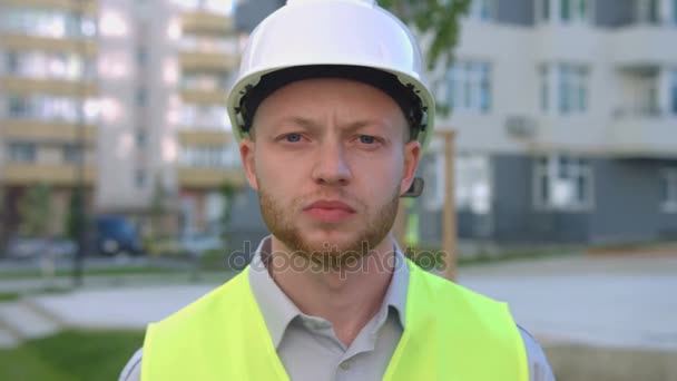 Portrait of serious caucasian builder with beard in the protective helmet looking to the camera. Outdoor. - Imágenes, Vídeo