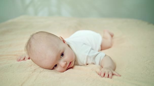 Bebé acostado boca abajo sobre una suave ropa de cama sonriendo
 - Imágenes, Vídeo