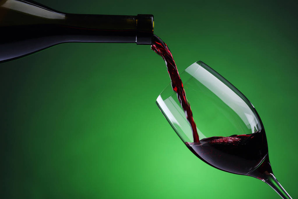 Rotwein in Weinglas auf grünem Hintergrund gießen - Foto, Bild