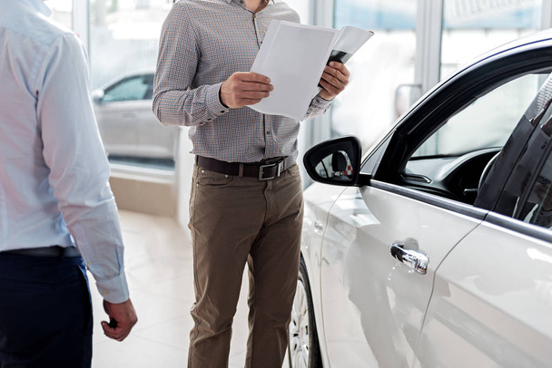 Visitor looking through agreement in car dealership - Valokuva, kuva