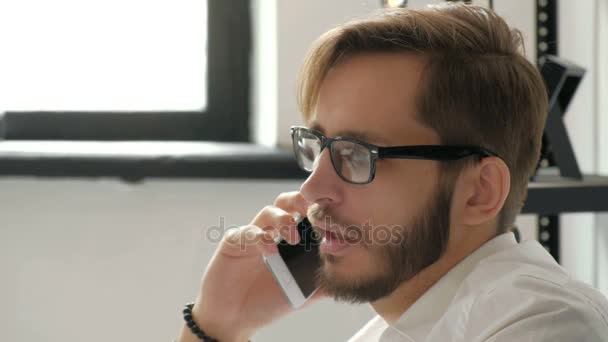 Attractive european guy talking on phone while using laptop at workplace 20s 4k. - Video