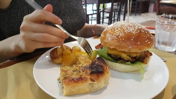 Νεαρή γυναίκα τρώει πατάτες και χάμπουργκερ στο εστιατόριο - Πλάνα, βίντεο
