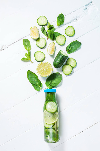 Cold and refreshing infused detox water with lime, mint and cucumber in a bottle on white wood background - Photo, Image