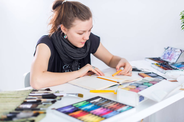 Jonge vrouwelijke artiest tekenen schets schetsboek met potlood op haar werk in de studio. Kant weergave portret van geïnspireerd schilder. - Foto, afbeelding