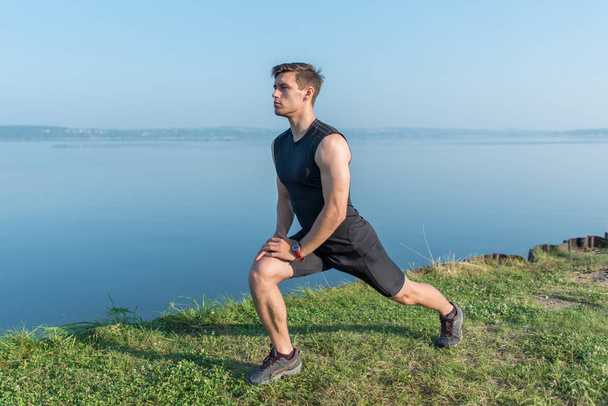 Young fit man stretching legs outdoors doing forward lunge. - Photo, Image