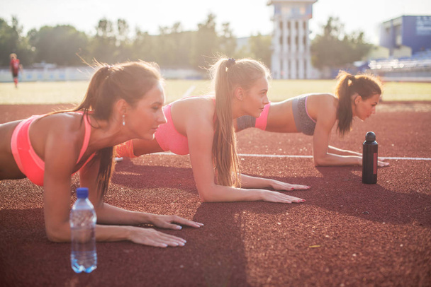 Vue latérale de jeunes belles femmes en tenue de sport faisant planche
. - Photo, image