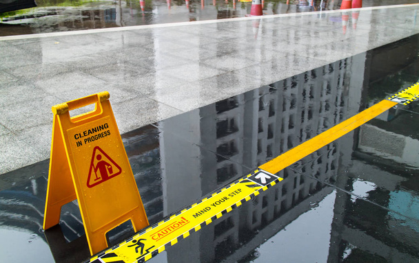 Πινακίδα που δείχνει την προειδοποίηση της προσοχής σε βρεγμένο δάπεδο και το μυαλό στο βήμα μπροστά από το κτίριο - Φωτογραφία, εικόνα