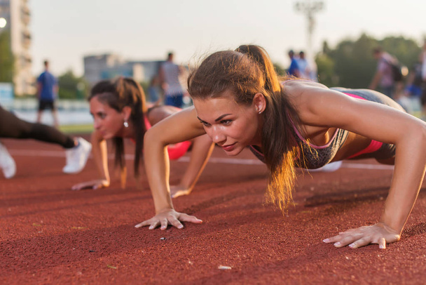 Push-ups athlete fitness women exercising in stadium. Training outdoors - Photo, Image