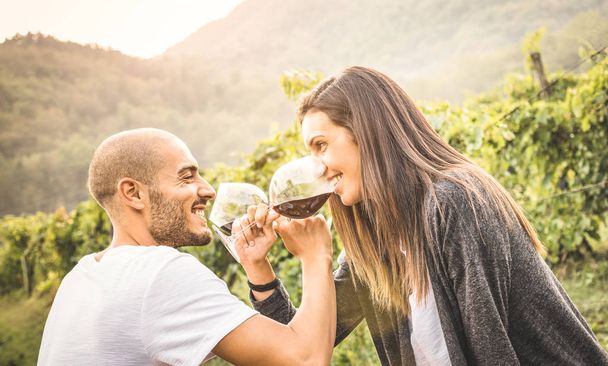 glückliches junges Liebespaar trinkt Rotwein auf dem Weingut - schöner Mann blickt in schöne Frauenaugen - alternatives Beziehungskonzept mit Freund und Freundin, die zusammen Spaß haben - Foto, Bild