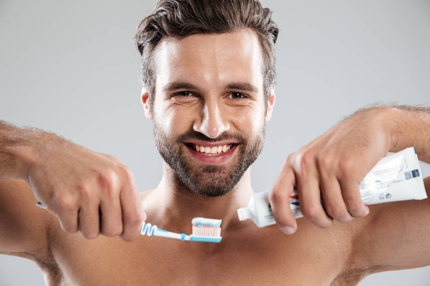 Portrait of a smiling man putting toothpaste on a toothbrush - Foto, immagini