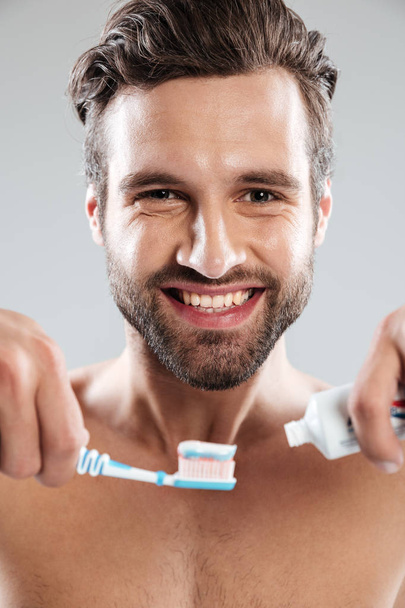 Portrait of a smiling man putting toothpaste on a toothbrush - Фото, изображение