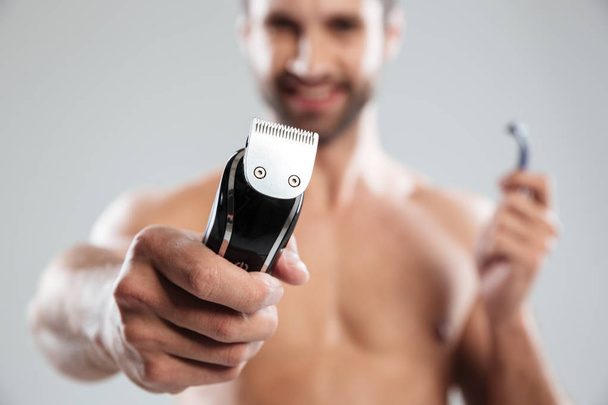 Portrait of a happy smiling bearded man showing electric razor - Foto, afbeelding