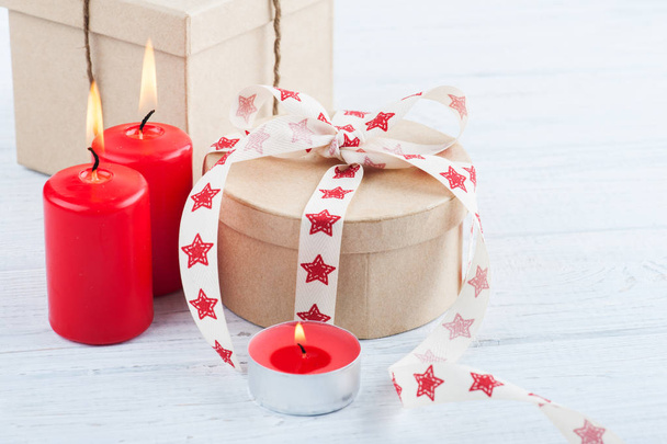 Gift in kraft box with red stars ribbon, lit candles and heart - Photo, Image