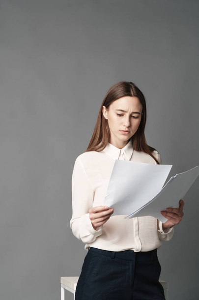 Businesswoman holds the papers in her hands and reads what is written there. Isolated on gray background. - Photo, Image