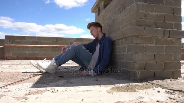 Young red-haired man hides from the sun in the shade on the roof. - Záběry, video