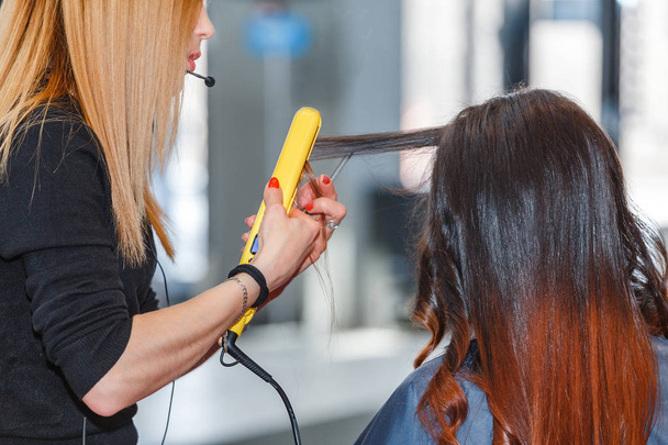 Zbliżenie na salon fryzjerski prostowania lub curling długie, czarne włosy z żelazka do włosów. - Zdjęcie, obraz