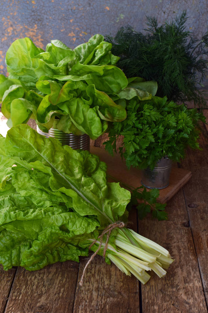 Σύνθεση πράσινα μυρωδικά και λαχανικά. Μίγμα οργανικών άνοιξη για σαλάτα με καφέ ξύλινη φόντο. Μαρούλι, άνηθο, μαϊντανό, σέσκουλα. - Φωτογραφία, εικόνα