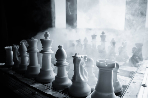tablero de ajedrez concepto de juego de ideas de negocios y la competencia y las ideas de estrategia cóncep. Figuras de ajedrez sobre un fondo oscuro con humo y niebla y ventana con luz solar
. - Foto, imagen