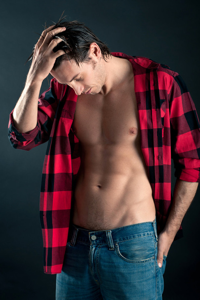Relaxed young man with plaid shirt against dark background - Фото, изображение