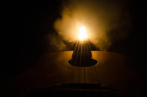 Concepto musical. Guitarra acústica aislada sobre un fondo oscuro bajo haz de luz con humo con espacio de copia. Cuerdas de Guitarra, de cerca. Enfoque selectivo. Efectos de fuego
 - Foto, imagen