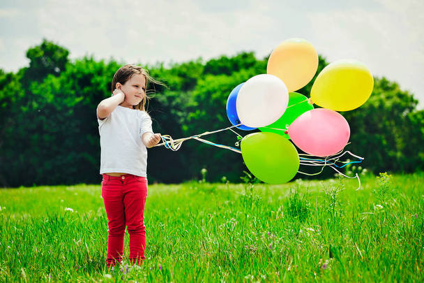 Маленька дівчинка з повітряними кулями в полі
 - Фото, зображення