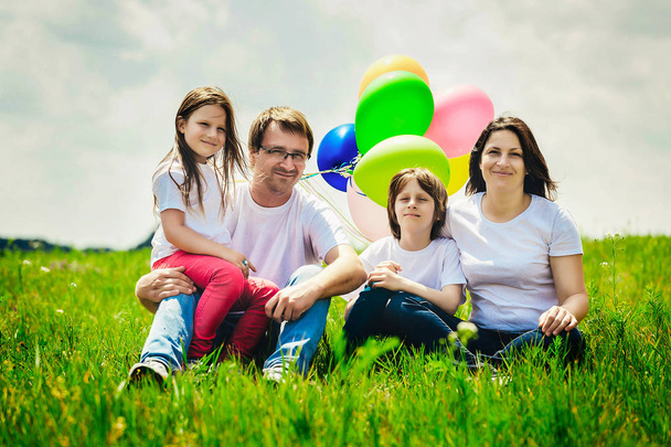 familia feliz sentado con globos al aire libre en un cálido día de verano
. - Foto, Imagen