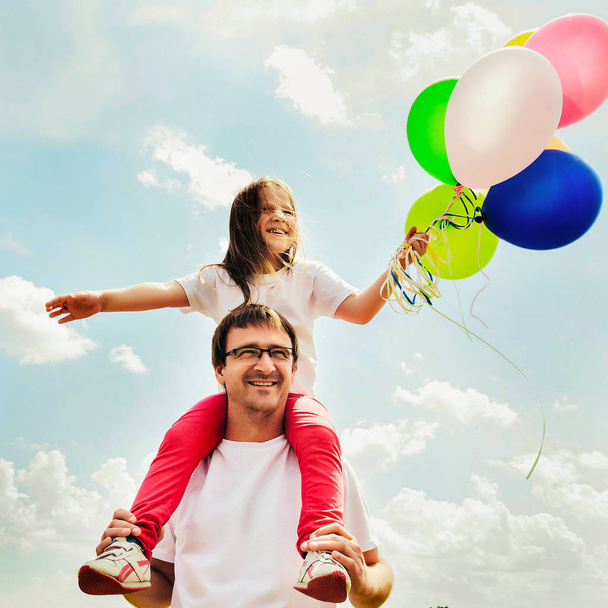 щаслива сім'я сидить з повітряними кулями на відкритому повітрі в теплий літній день
 - Фото, зображення