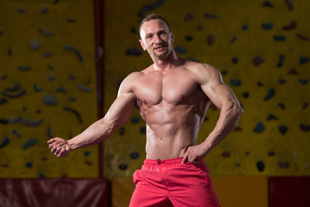 Komea lihaksikas mies flexing lihaksia kuntosalilla
 - Valokuva, kuva