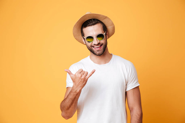 Lächelnder Mann mit Sommermütze blickt Kamera isoliert gestikulierend - Foto, Bild