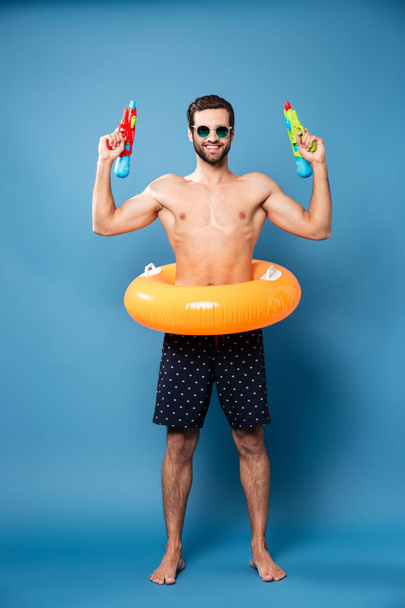 Cheerful man looking camera while holding water guns isolated - Foto, Imagem