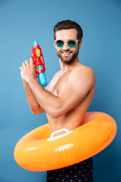Portrait of cheerful man looking camera with water gun - Фото, зображення