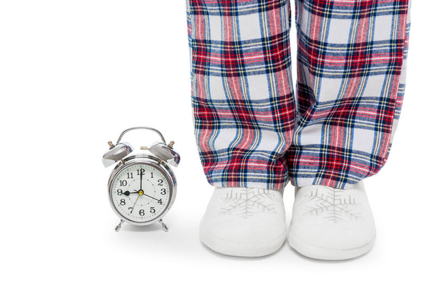 Alarm clock and female legs in pajamas and slippers on a white b - Photo, Image