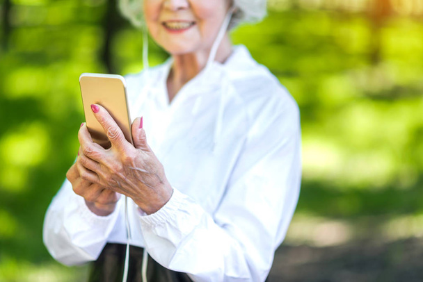 Happy elderly lady using cellphone while exercising outdoors - Zdjęcie, obraz