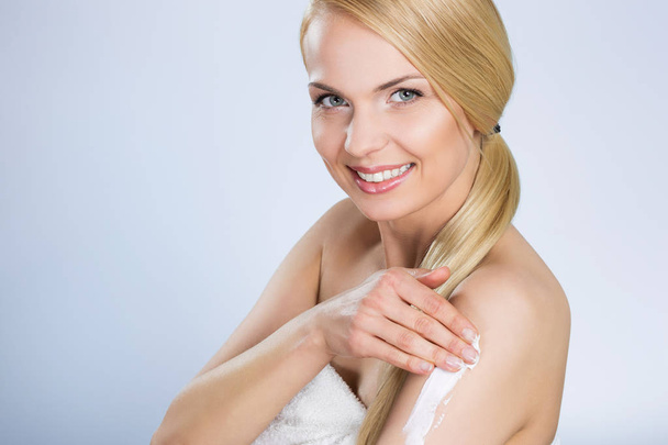 Beautiful happy woman applying cream on arm - Foto, afbeelding