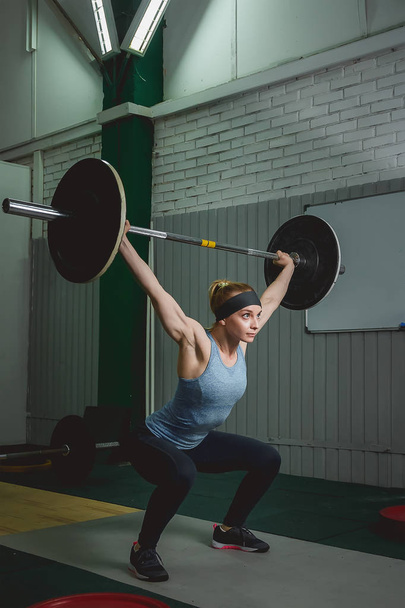 Strong woman lifting barbell as a part of crossfit exercise routine - Foto, imagen